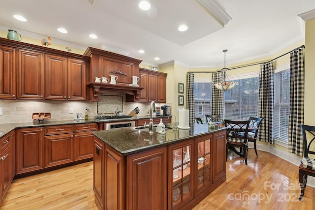 kitchen with sink, dark stone countertops, decorative light fixtures, a center island with sink, and light wood-type flooring