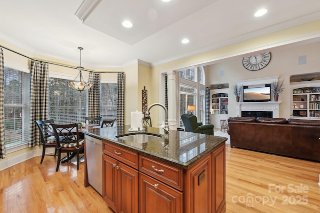 kitchen with stainless steel dishwasher, sink, decorative light fixtures, dark stone countertops, and an island with sink