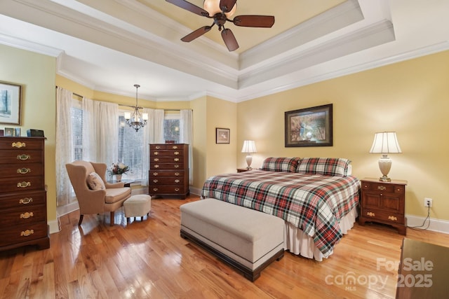 bedroom featuring hardwood / wood-style flooring, ceiling fan with notable chandelier, a raised ceiling, and ornamental molding