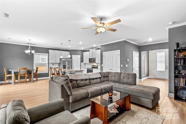 living room with ceiling fan with notable chandelier, light hardwood / wood-style flooring, crown molding, and sink