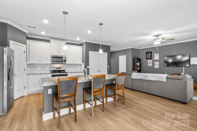 kitchen featuring stainless steel appliances, white cabinetry, hanging light fixtures, and a center island with sink