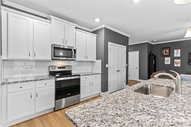 kitchen with appliances with stainless steel finishes, light wood-type flooring, tasteful backsplash, sink, and white cabinetry