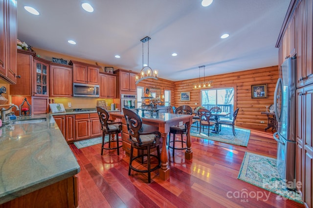 kitchen with decorative light fixtures, sink, appliances with stainless steel finishes, dark wood-type flooring, and log walls