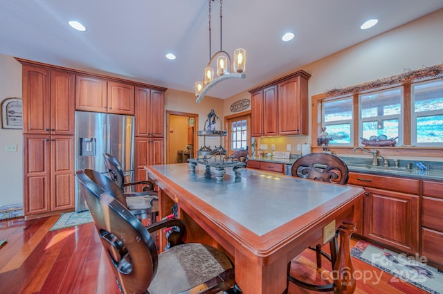 kitchen with pendant lighting, stainless steel refrigerator with ice dispenser, sink, an inviting chandelier, and hardwood / wood-style flooring