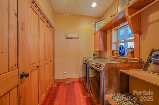 clothes washing area featuring cabinets, washer and clothes dryer, and dark hardwood / wood-style flooring