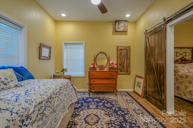 bedroom featuring ceiling fan, a barn door, and hardwood / wood-style flooring