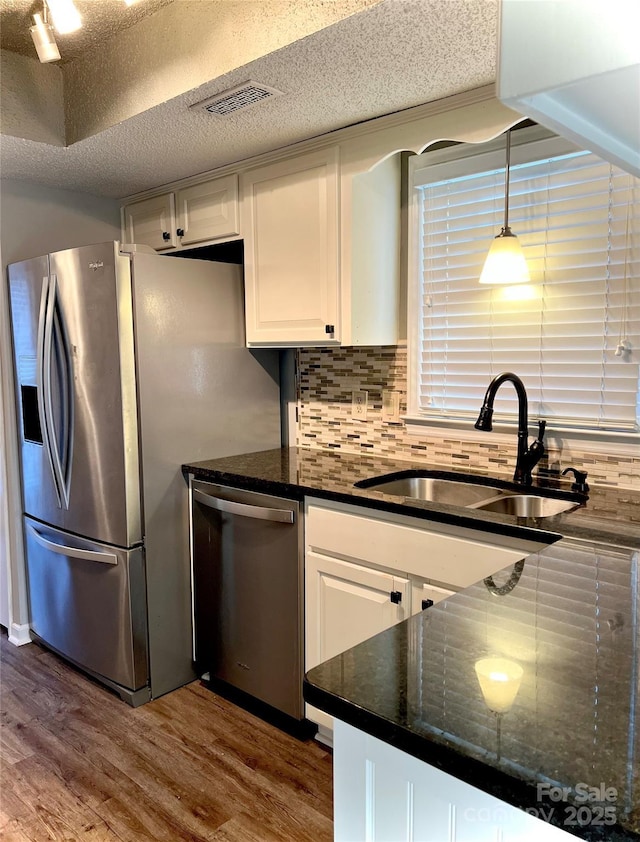 kitchen featuring backsplash, hanging light fixtures, sink, appliances with stainless steel finishes, and white cabinetry