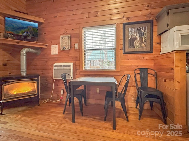 dining space with light hardwood / wood-style floors, a wood stove, a wall mounted AC, and wooden walls