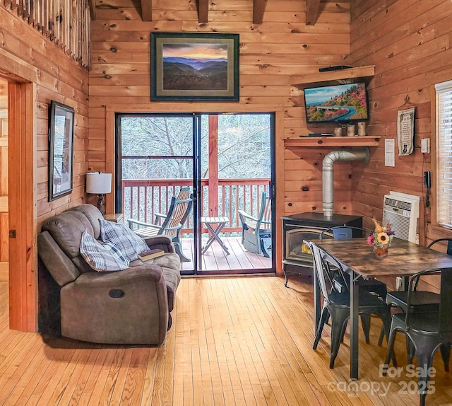 interior space with beamed ceiling, wooden walls, a wood stove, light hardwood / wood-style flooring, and a wall unit AC