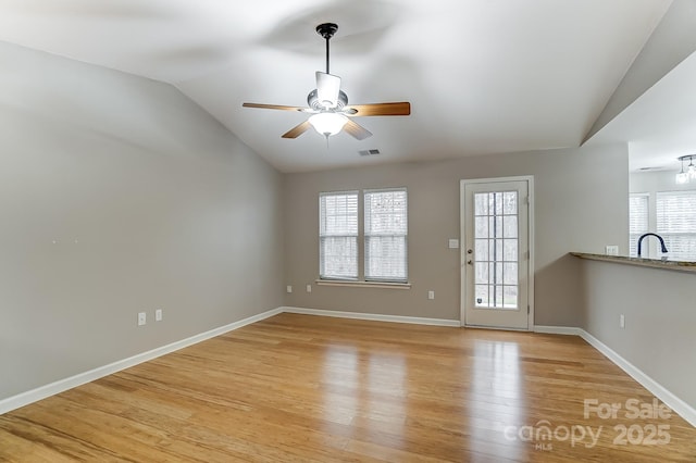 unfurnished living room with ceiling fan, sink, light hardwood / wood-style floors, and vaulted ceiling