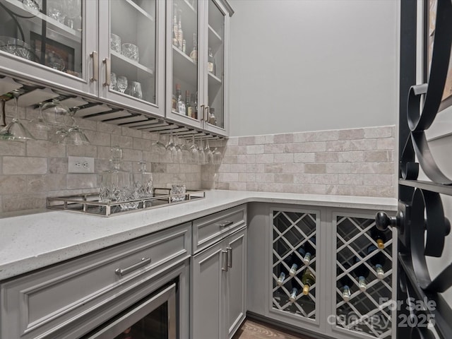 bar with light stone counters, gas stovetop, decorative backsplash, and gray cabinetry