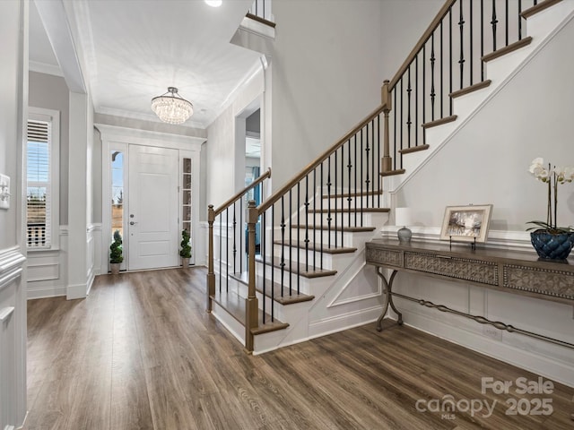 entryway with hardwood / wood-style flooring, crown molding, and a notable chandelier