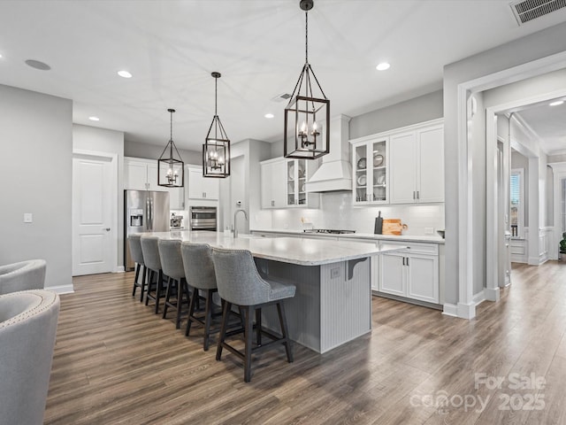 kitchen featuring hanging light fixtures, dark hardwood / wood-style flooring, an island with sink, stainless steel appliances, and white cabinets