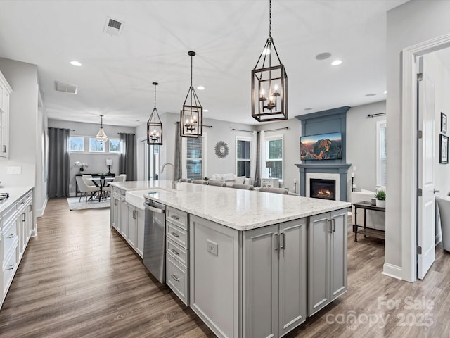 kitchen with decorative light fixtures, sink, gray cabinetry, a kitchen island with sink, and stainless steel dishwasher