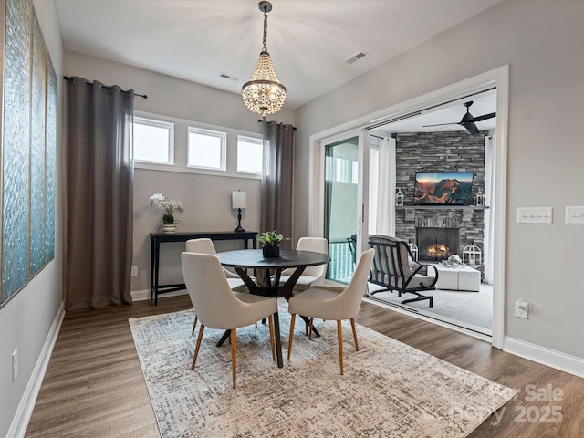 dining room with a fireplace, ceiling fan with notable chandelier, and wood-type flooring