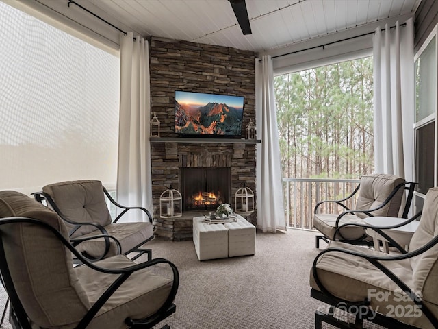 living area with a stone fireplace, carpet floors, wooden ceiling, and ceiling fan