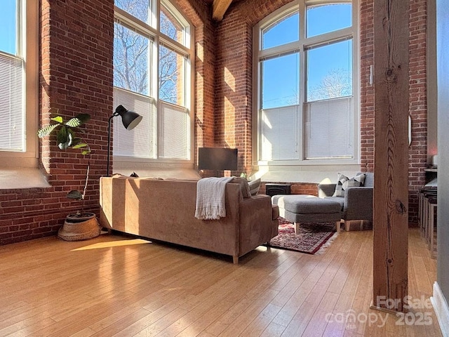 living room with beamed ceiling, light wood-type flooring, a high ceiling, and brick wall