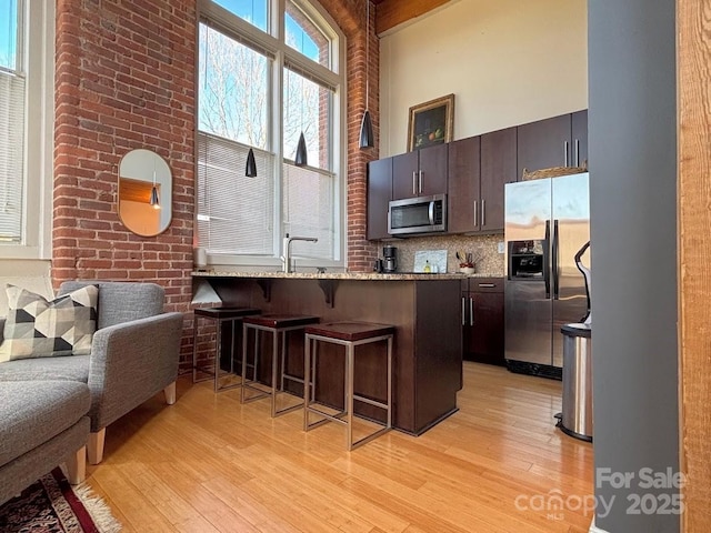 kitchen featuring kitchen peninsula, appliances with stainless steel finishes, a towering ceiling, a breakfast bar, and dark brown cabinets