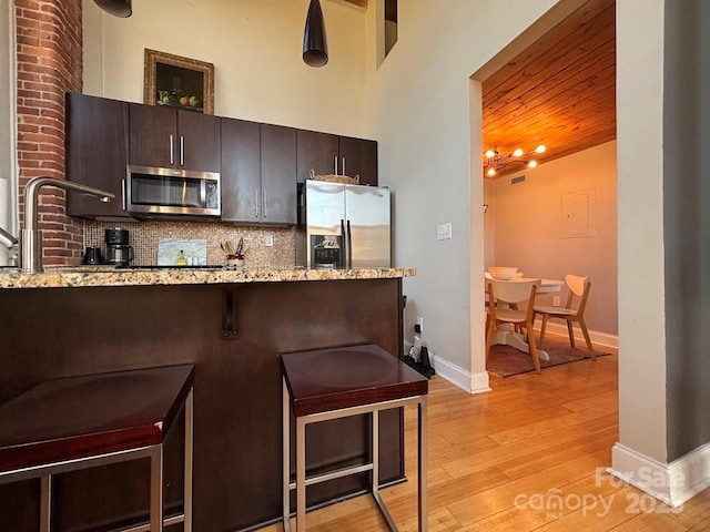 kitchen featuring light hardwood / wood-style flooring, decorative backsplash, dark brown cabinets, light stone counters, and stainless steel appliances