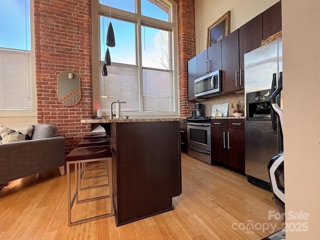 kitchen with light hardwood / wood-style flooring, appliances with stainless steel finishes, tasteful backsplash, a breakfast bar area, and brick wall