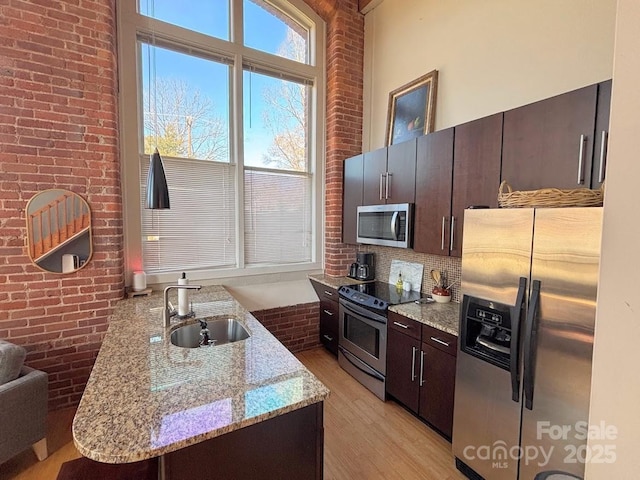 kitchen with light stone countertops, sink, stainless steel appliances, a towering ceiling, and dark brown cabinets