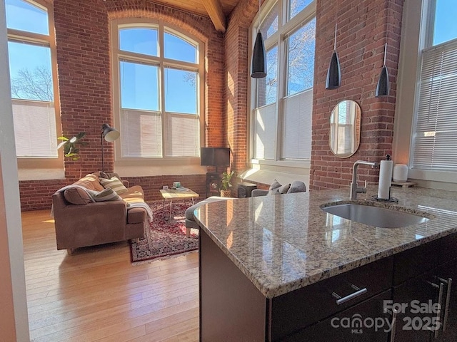 kitchen featuring light wood-type flooring, light stone countertops, sink, and brick wall