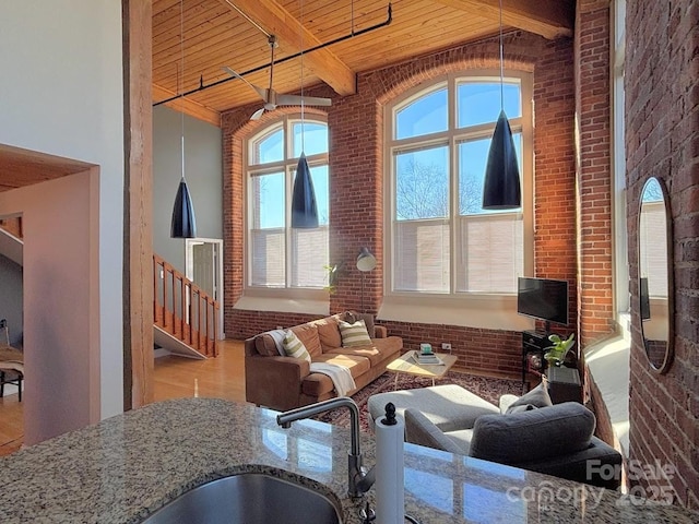 living room featuring beam ceiling, a healthy amount of sunlight, wood ceiling, and brick wall