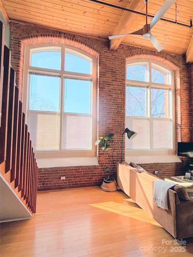 interior space featuring ceiling fan, wood ceiling, a healthy amount of sunlight, and brick wall