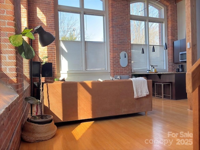 living room with a wealth of natural light, wood-type flooring, and brick wall