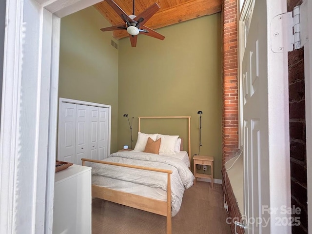 carpeted bedroom featuring beam ceiling, ceiling fan, a towering ceiling, a closet, and wood ceiling