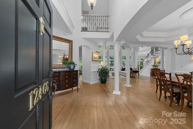 entrance foyer featuring decorative columns, crown molding, light wood-type flooring, and a notable chandelier