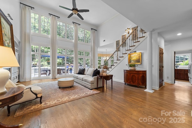 living room with crown molding, a high ceiling, ceiling fan with notable chandelier, and hardwood / wood-style flooring