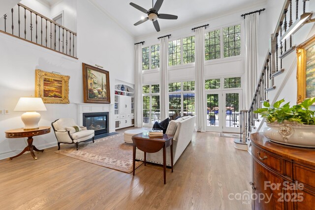 living room with a high ceiling, french doors, light hardwood / wood-style flooring, ceiling fan, and ornamental molding