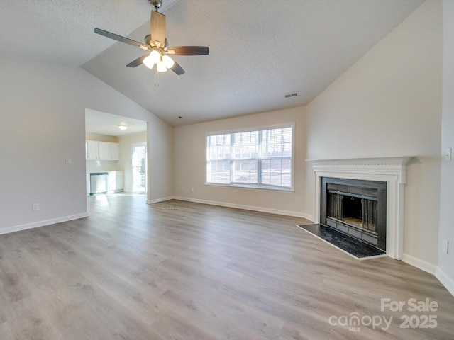 unfurnished living room featuring ceiling fan, vaulted ceiling, light hardwood / wood-style floors, and a textured ceiling