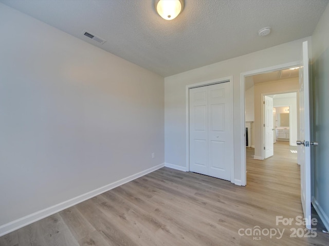 unfurnished bedroom with light hardwood / wood-style flooring, a closet, and a textured ceiling