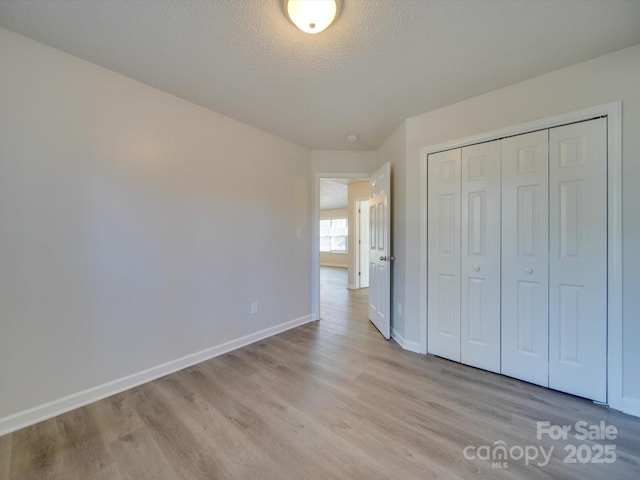 unfurnished bedroom featuring a closet, a textured ceiling, and light wood-type flooring