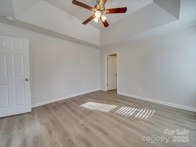 spare room with ceiling fan, lofted ceiling, a raised ceiling, and light wood-type flooring