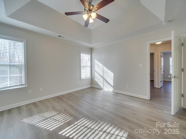 empty room with crown molding, a tray ceiling, ceiling fan, and light wood-type flooring