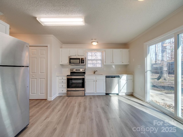 kitchen with stainless steel appliances, white cabinetry, ornamental molding, and light hardwood / wood-style flooring