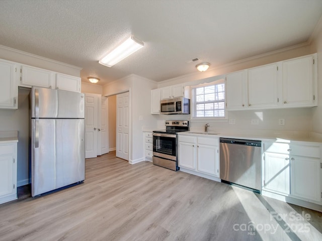 kitchen with sink, white cabinetry, light hardwood / wood-style flooring, ornamental molding, and appliances with stainless steel finishes