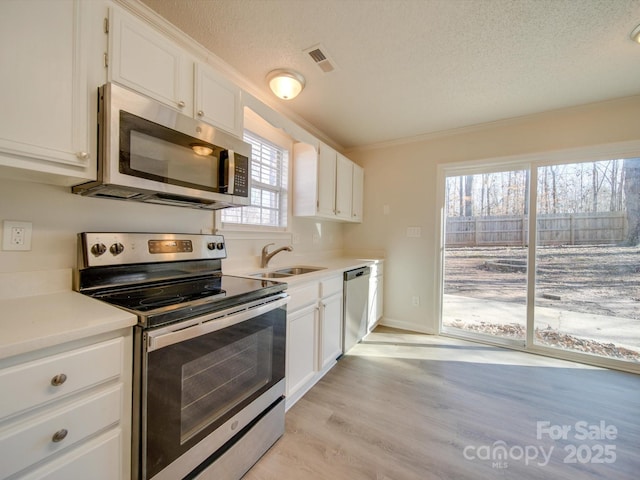 kitchen featuring sink, appliances with stainless steel finishes, light hardwood / wood-style floors, a textured ceiling, and white cabinets