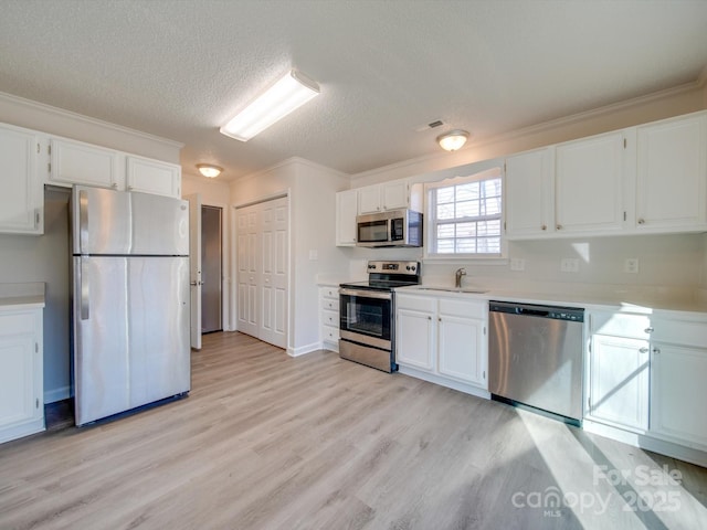 kitchen with ornamental molding, stainless steel appliances, light wood-type flooring, and white cabinets