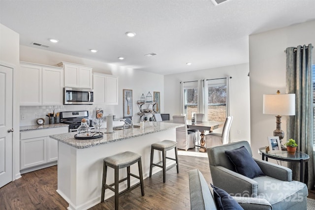 kitchen featuring decorative backsplash, stainless steel appliances, dark wood-type flooring, a center island with sink, and white cabinets