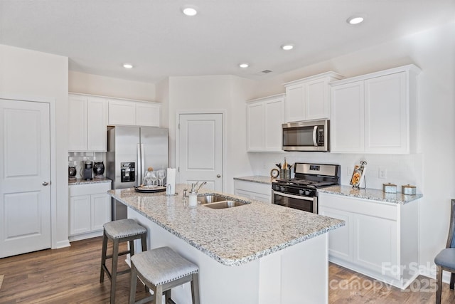 kitchen with appliances with stainless steel finishes, a kitchen island with sink, sink, hardwood / wood-style flooring, and white cabinetry