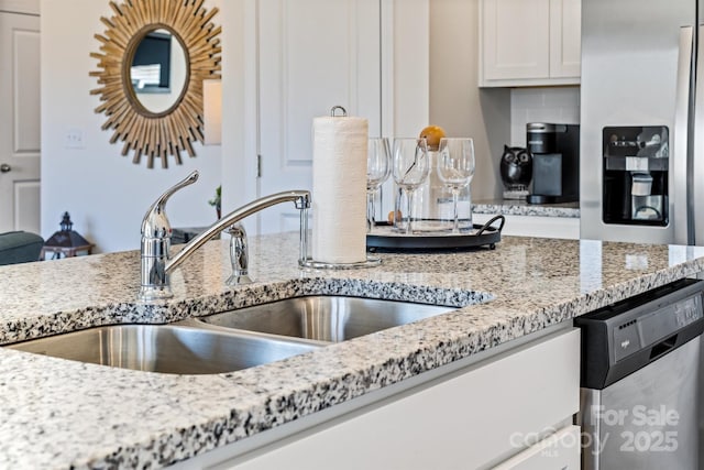 kitchen featuring light stone countertops, white cabinetry, sink, and stainless steel dishwasher