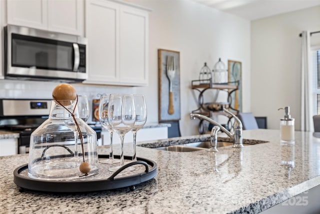 kitchen with decorative backsplash, white cabinetry, stove, and light stone counters