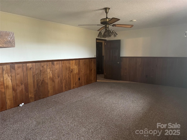 carpeted spare room with ceiling fan, wooden walls, and a textured ceiling