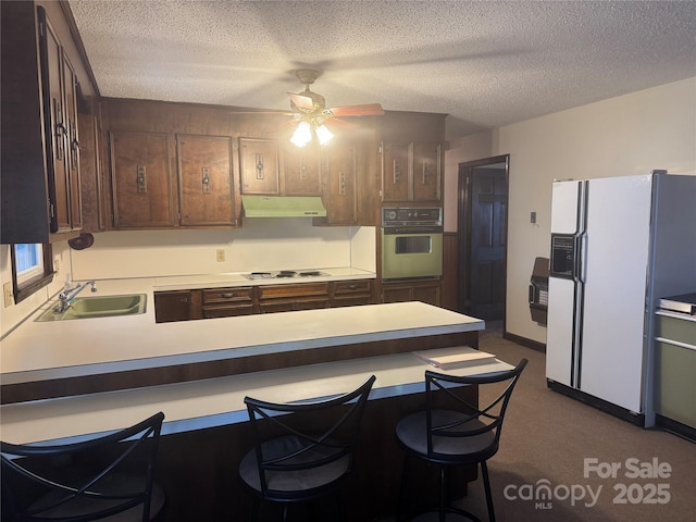 kitchen with sink, white appliances, a textured ceiling, a kitchen bar, and kitchen peninsula