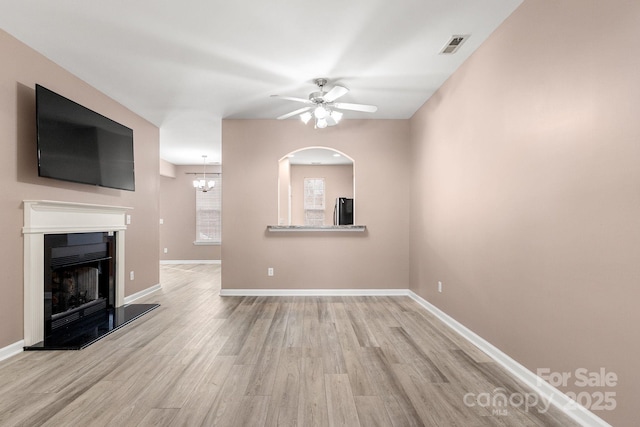 unfurnished living room featuring ceiling fan with notable chandelier and light hardwood / wood-style flooring