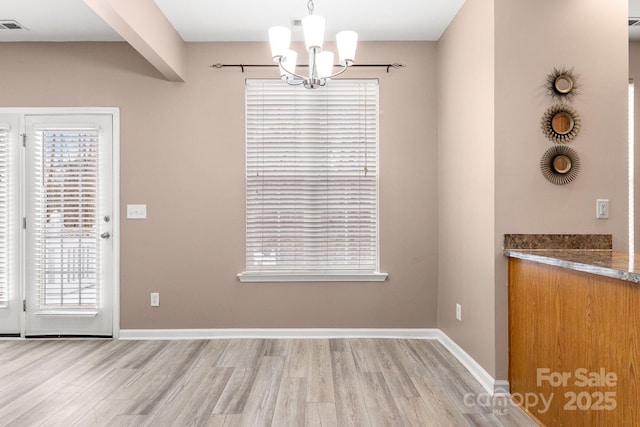 unfurnished dining area with light hardwood / wood-style floors and a notable chandelier